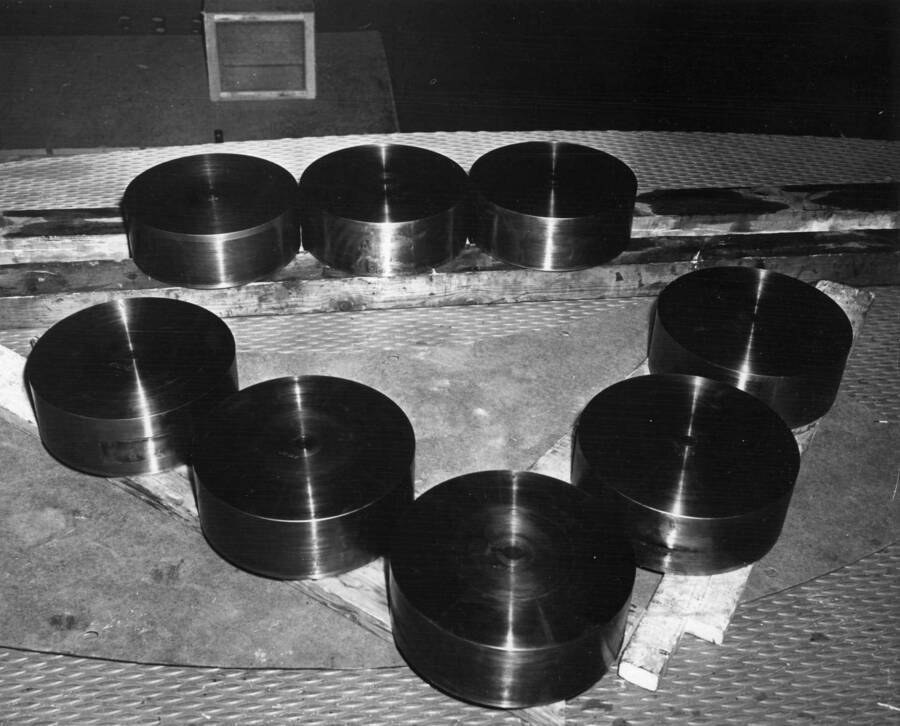 View of eight thrust bearing discs for unit L-3. The discs are laying upside down to indicate worn spots in the centers where the jack screws had made contact. The depth of these holes varied from 0.005' to 0.007' Grand Coulee Power Plant--Columbia Basin Project.