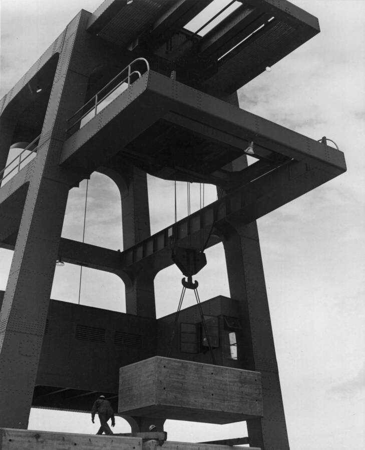 One hundred fifty ton gentry crane being tested. Crane is lifting a thirty-seven and one half ton concrete block. This machine was built by Star Manufacturing Company of Tacoma, Washington and is installed on tracks reaching across the top of the dam.
