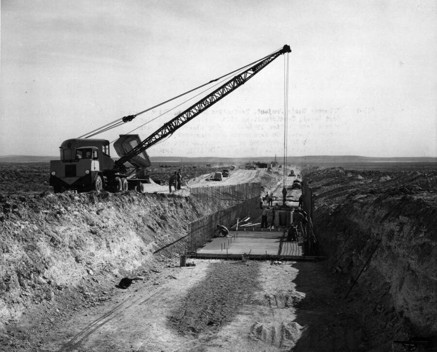 Columbia Basin Project, Irrigation Division, Third Section West Canal, Specifications 2844, Schedule 3. Looking downstream from station 1992+45 showing placement of concrete at approximate Station 1993+40 and placement of reinforcement steel at approximate Station 1994+50 and road grader back can be seen in the contractor's field camp. *This patrol is fine grading the subgrade. Hinnin and Schilling--Contractor. H.E. Foss, photographer.