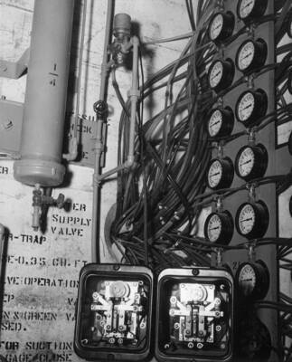 North Coulee Dam, Piezometer Terminal Well, A view of the piezometer test apparatus at the corner of the upstream and right walls of the well. The pore pressure in the dam embankment and foundation are transmitted through the water-filled tubes and recorded on the Bourdon tube pressure gages at the right. The solenoid operated valve at the top transmits pulsating waves through the system to assist in the removal of air in the tubes. Two TK Westinghouse relays at the bottom are electrically connected in series with the solenoid valve. Any cycle desired for the operation of solenoid valve can be obtained by adjustments of the timing devices in the relays. The air trap at the upper left supplies water and removes air from the system. Specifications 2586, Contract I2r-18481, J.A. Terteling and Sons, Inc., Contractor.
