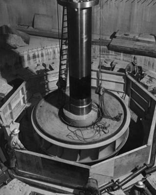 Col. Basin Proj., Grand Coulee Dam.--Lowering the turbine runner for the No. 1 Shasta Dam generator, of 75,000 kw. Capacity, moved to Grand Coulee Dam with another machine of like size to expedite delivery of new power to Pacific Coast war industries. The wheel is seen as it is entering the well at el. 979. The weight of the runner with its 41 1/2' shaft is about 85 tons.