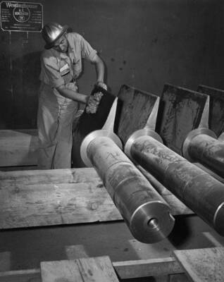 Huge wicket gates stored on generator deck is wiped off by H.R. Ramm, U.S.B.R. foreman.
