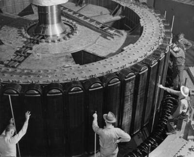 A tight fit. The clearance between the huge 25-foot rotors and the stators of the two 75,000 kilowatt Shasta Dam generators, being installed at Grand Coulee Dam to make additional power available for war industries, is only 5/8 inch. Lowering this 450 ton wheel into place, the operators of the two powerhouse cranes, that jointly supported the load, were guided by workmen, stationed around the rim, who inserted sticks between the stationary and moving parts to measure the clearance and prevent contact. When the unit goes into service next February, the outer rim of this rotor, which is 7 feet high, will spin at 125 miles per hour. Attached to the rim are 52 magnets, weighing 3300 lbs. each.