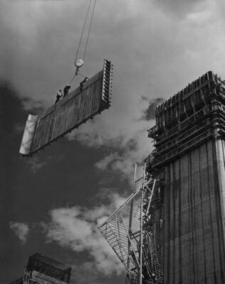 Hoisting elevator shaft form into place. 3 men riding load.