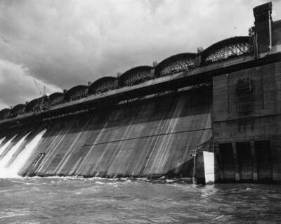 View of a portion of the spillway section showing formwork and falsework for construction of spillway bridge spans. The construction trestle appears below the formwork. Eight of the 102-inch outlet tubes are shown in use for diversion of the river flow (right)