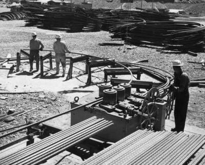 Columbia Basin Project, Irrigation Division, Soap Lake Siphon, Specifications No. 2411, Winston Brothers and Utah Construction Co., Contractors. This photograph is a close-up of the fabrication of the half hoops. The straight bar is fed to the machine from the lower left, goes through the rolls, and follows the support rollers around the upper left. H.E. Foss, photographer.