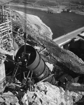 Specifications 2329. Contractor: Morrison-Knudsen Company, Inc. and Peter Kiewit Sons' Company. Subcontractor: Consolidated Western Steel Corporation. Progress view of 12-foot diameter pump-discharge pipe emerging from P-4 tunnel. The two top 20-foot lengths are seen to be 'fitted up' and ready for welding. The two men within the end of the pipe are on a wheel mounted welding jumbo used to make welds on the inside pipe seams. Forming and scaffolds to the right are for the anchor block of the P-3 pipe.