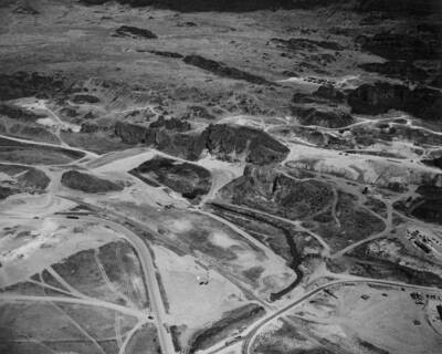 An aerial view of the site of North Coulee Dam which extends from the stripped area at the lower left hand corner to the large basalt rock in the center of the picture. The power shovel is working approximately at the center of the proposed earth dam