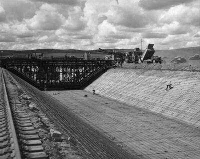 West Canal, Specs. 1286, Winston-Utah Co. Guntert and Zimmerman lining machine in operation. At the right are the two tractor-propelled mixers which serve the paver. A truck is dumping aggregates and cement in the hopper of the mixer. Photo by F.B. Pomeroy