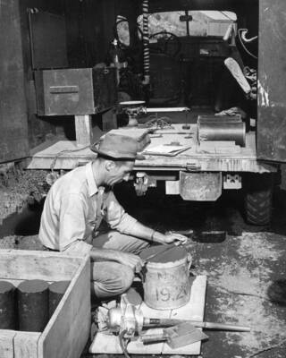 Columbia Basin Project--Irrigation Division. East Low Canal--Specifications No. 1422. View of mobile laboratory used to make test cylinders and air entrainment tests of canal lining concrete. Equipment shown includes half-cubic foot unit weight measure, electric vibrator, scale, and gasoline-powered generator. In left foreground is covered box where test cylinders are stored until picked up on the following day. Cylinders from previous day's test may be seen in ambulance used for transportation. H.E. Foss, photographer.