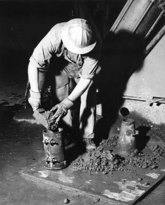 Govt. inspector filling cylinder with concrete sample at a plant for compression braking test