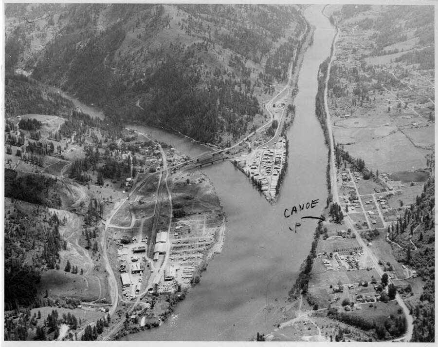 A nice view of Ahsahka & the forks of the river. Note on back: "" Note the work by Murphy Bros. of  Spokane has just started in the construction of the access road up to dam site. See the clearing on the left. Ahsahka mill, lower, and Orofino in the distance, upstream on upper right. Canoe camp is marked by wax pencil. This is where Lewis and Clark stopped in 1805 and changed their horses for canoes to continue their trip to the mouth of the Columbia. This is now a part of the Nez perce Historical Park. Bet they never thought of a dam when they were there.  (A. B. Curtis)""