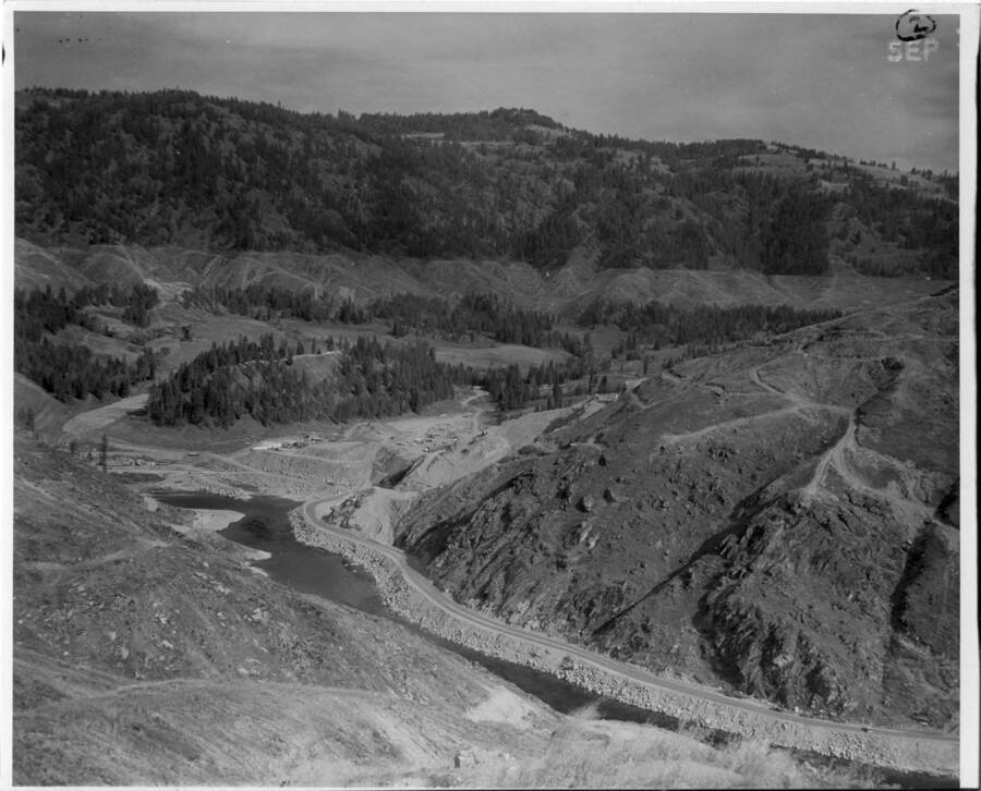 During early construction stages a road was built up the south side of the river to the contractors shops location. Note on back: "" Land clearing has started at elevation 1605 on the distant hills. This will be the pool level.""