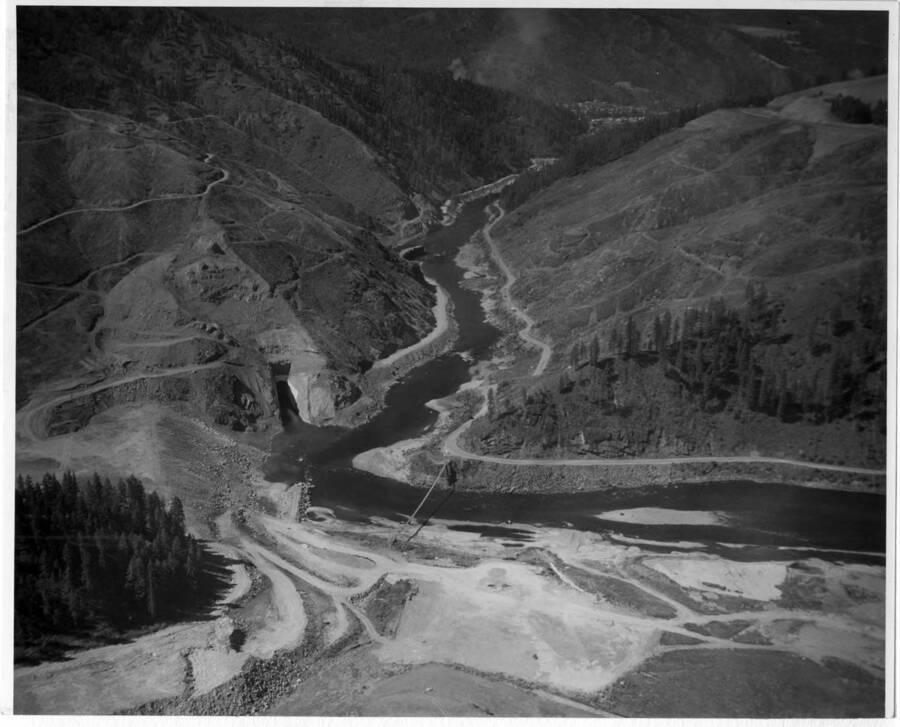 Dam site and diversion tunnel has been started from both ends. Note on back: ""The tunnel met exactly in the middle of the ridge. You can see the coffer dam just being started on the lower end and Orofino is in the distance. Clearing has been done on both sides. Murphy Bros. has built the road.""