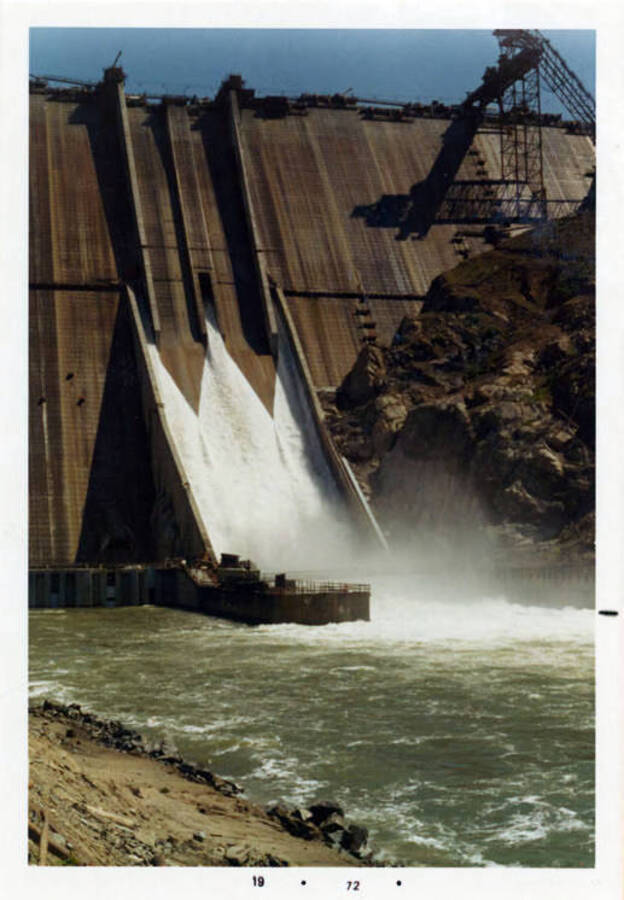 Photograph showing the spillway in full operation & the top of the dam.  About 100 ft. to go to top it out.