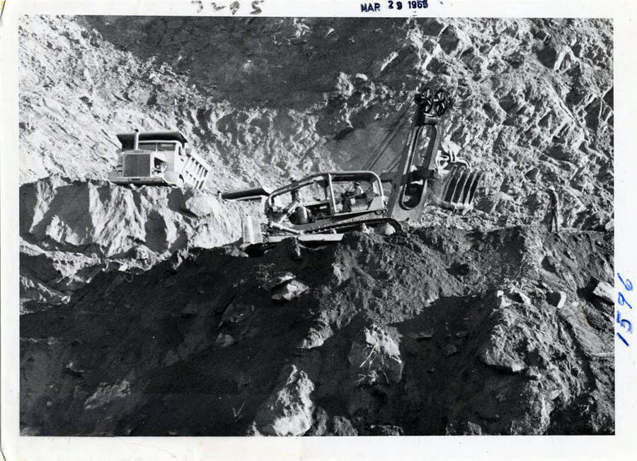 Photograph of the early work in the rock pit at the dam.  The heavy equipment doing the work are a large dump, a dozer and the big shovel.  This rock pit was opened up, granite, for fill material, the coffer dam and then the material to make concrete.