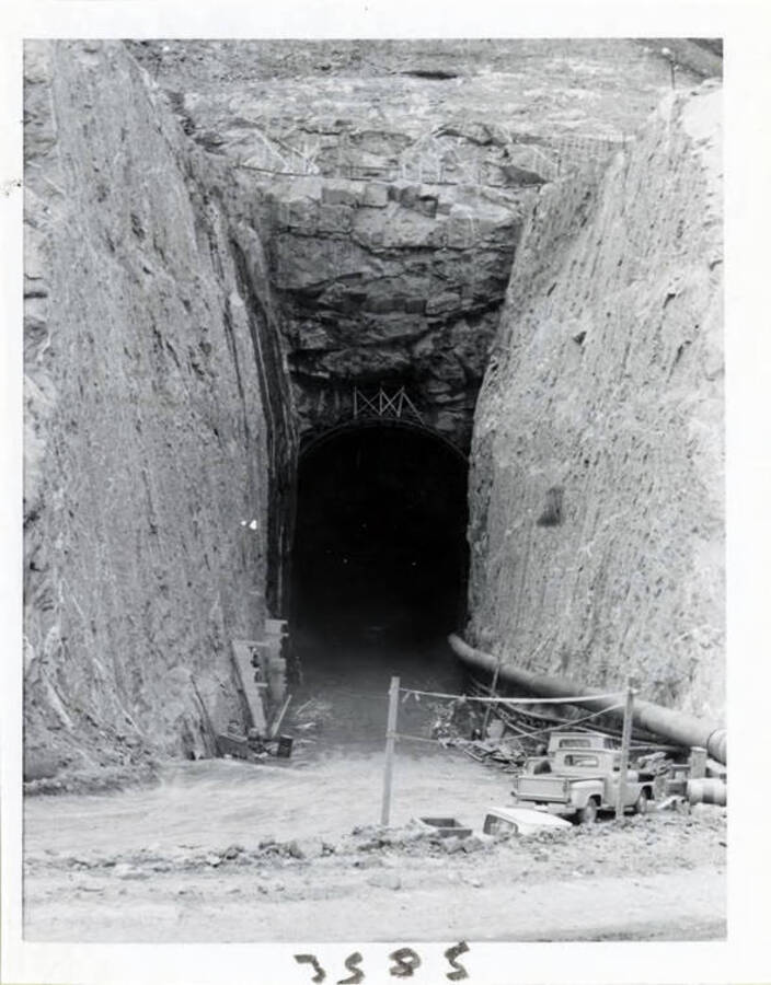 Photograph shows the diversion tunnel under construction.  You will note on the right hand side the air line going in to operate the jack hammers.  Also, the road to haul out the rock as it was drilled and blasted.