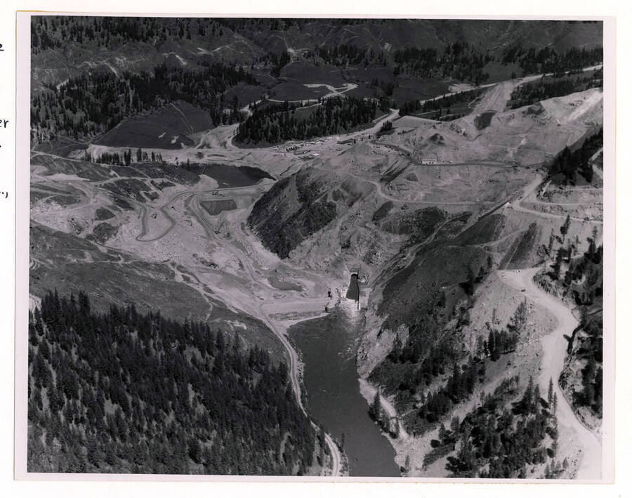 Photograph showing the construction site up and down stream from cofferdams in place and diversion of North Fork of Clearwater River flowing through a tunnel.