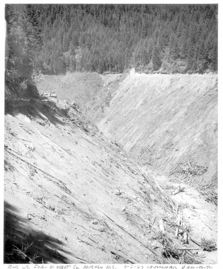 Yoyo operation - cable from upper cat is tied to other cat so he can crawl back up hill. Note on margin of image: ""Elk Cr. Job - H. West Co. Murphy N.C. 8-3-67 - Dworshak Dam -Yo -yo"". Note on back: ""Same job, same place, same day as #702 & 703. This shows what you do on steep country, where you may turn a cat over and kill a person. Very dangerous. You will note here that two cats are working together. This they call a yo-yo operation. The cable from the upper cat is tied to the cat so that he can crawl back up the hill and make another pass down the hill with debris. They had to work together for safety.""