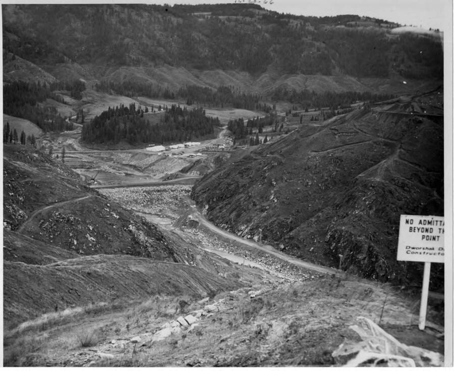 Coffer dam under construction. The, road up the south side of river to it & the clearing before the key way was started. Note on back: ""The buildings in the background are the contractors shops. This was all flooded out, of course, it is upstream from the dam.""