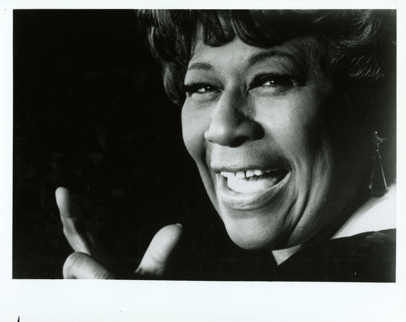 Black and white photographed portait of Ella Fitzgerald smiling at the camera.