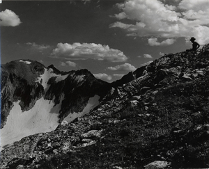 A man sits atop a mountain looking out towards a valley.