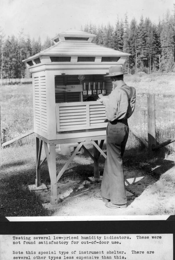 Testing several low-priced humidty indicators. These were not found satisfactory for out-of-door use. Note this special type of instrument shelter. There are several other types less expensive than this. This is a Hazen instrument shelter and still in use at Priest Creek Experimental Forest. Pictured is Joy Armstrong.