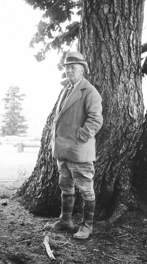 An identified man stands for a photograph in front of a tree in an unknown location, most likely the Priest River Experimental Forest.