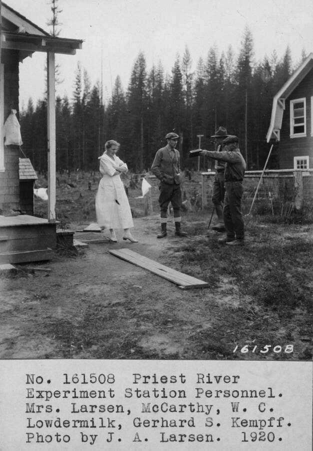 Filed in Priest Creek Experimental Forest Photo box #4: Priest River Experimental Station Personnel. Mrs. Larsen, McCarthy, W.C. Lowdermilk, and Gerhard Santorium Kempff between cottages 1 and 2, Priest River Experimental Station, 1920.  Kempff and Mac arguing as usual