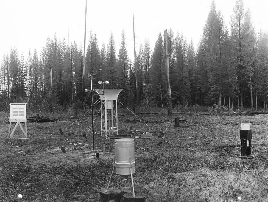 Plate XV caption: "Control meteorological station on Benton Flat, Priest River Experimental Station.  In backgroound an even-aged stand of 50 year old western larch. Situation representative of the larch type of northwestern Montana and Idaho."  The instruments were moved from this site to their present location next to Office in 1916.