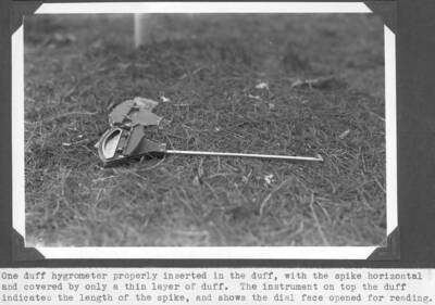 One duff hygrometer properly inserted in the duff, with the spike horizontal and covered by only a thin layer of duff. The instrument on top the duff indicated the length of the spike, and shows the dial face opened for reading.