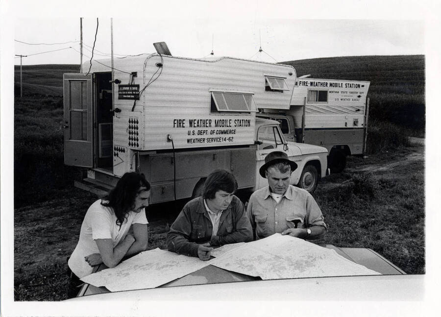 DDT Spray Project Douglas Fir Tussock Moth: Lyon, James; Crowe, John; Emerson, Ellis. The men are reading two maps. The writing on the truck reads: 'Fire Weather Mobile Station U.S. Dept. of Commerce Weather Service 14-62'.