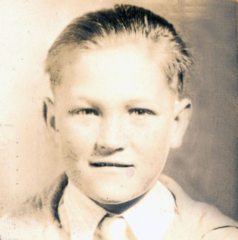 A young boy with neatly combed hair is wearing a shirt and tie, facing forward with a neutral expression.