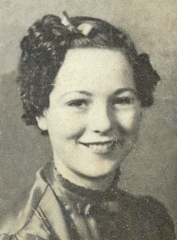 A woman with curly hair wearing a shiny blouse, smiling and looking straight ahead.