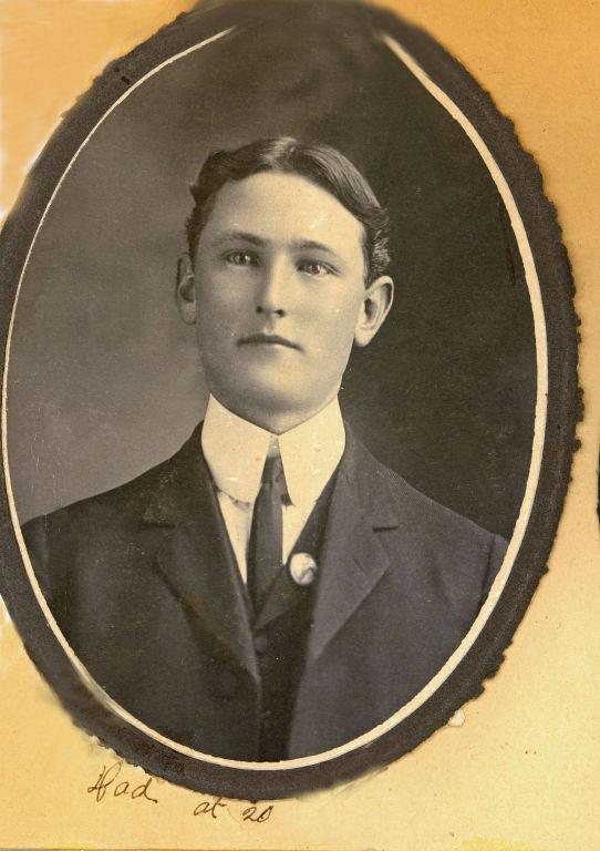 A young man in a formal suit and tie is shown from the chest up, with neatly styled hair. The portrait is surrounded by an oval border. Handwritten text below reads: "Dad at 20."