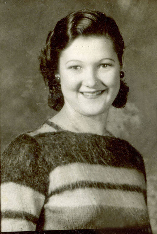 A person with short, wavy hair and a friendly smile, wearing a striped sweater and earrings, is posed against a neutral background.