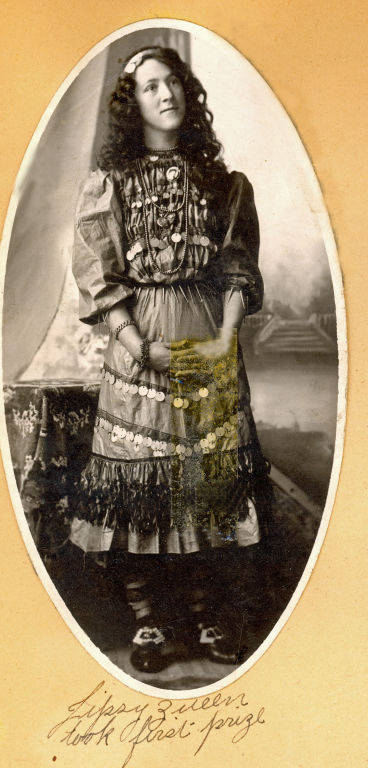 A woman is standing, wearing a detailed patterned dress adorned with what appear to be coins. Her hair is curly and long. The image has an oval frame. Below her, handwritten text reads, "Gypsy Queen took first prize."