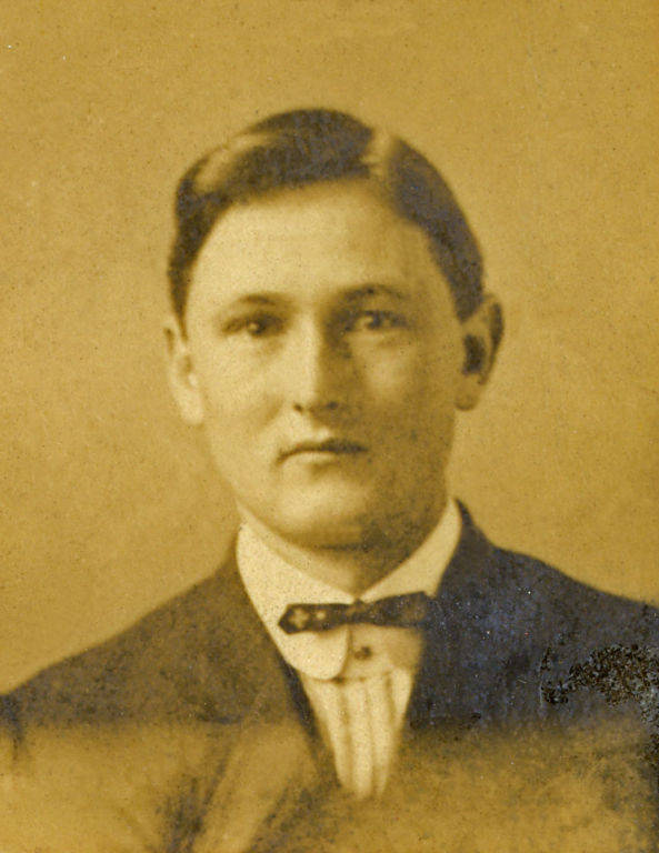 A man with short hair is wearing a suit, a collared shirt, and a bow tie. He looks directly at the viewer.