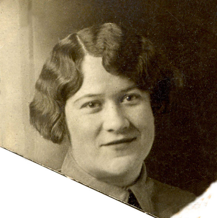 A person with short, waved hair is looking towards the camera. They are wearing a collared shirt and a tie.