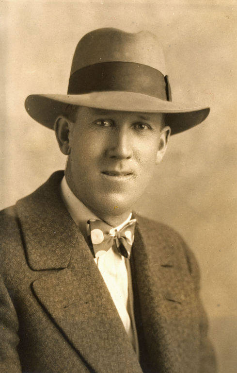 A man wearing a suit, bow tie, and hat, looking forward.