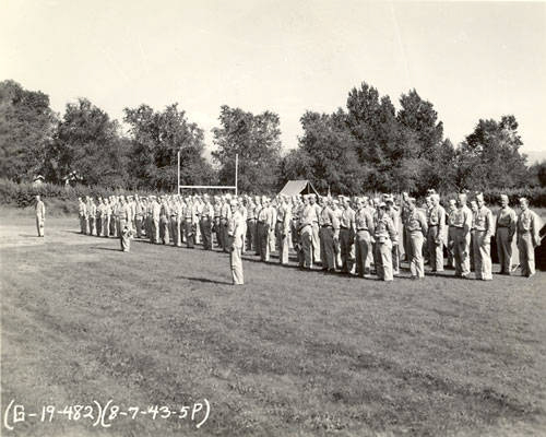 A group of uniformed soldiers standing in formation on a grassy field, with trees and goalposts in the background. The numbers and date "(G-19-482) (8-7-43-5P)" are written in the lower left corner.