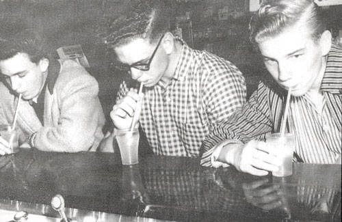 Three young men sitting at a counter, each sipping a drink through a straw.