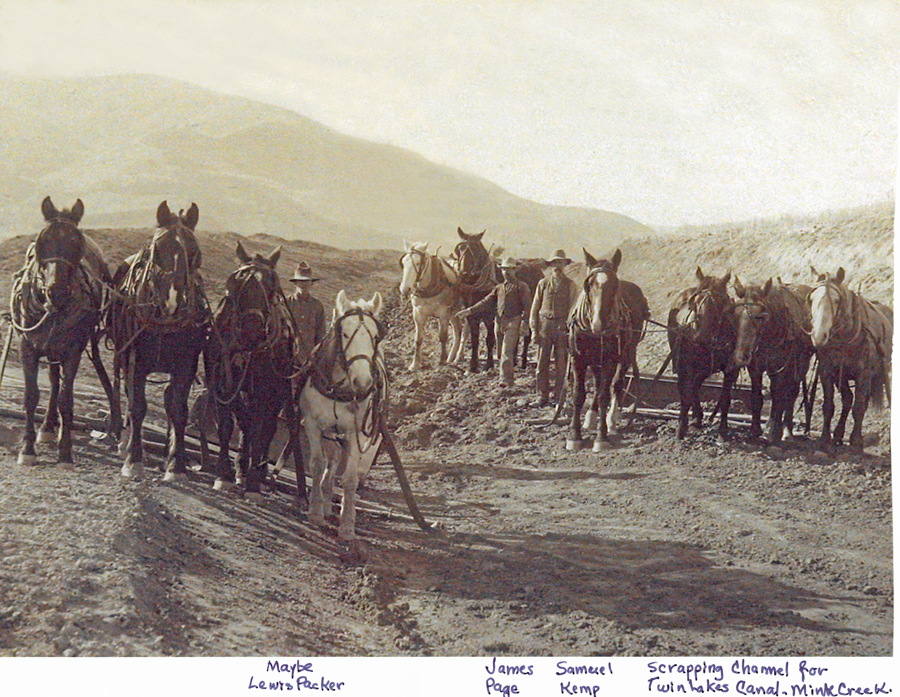 A group of men standing with a team of horses on a dirt path. Each man is holding horse reins. The background features hills. Below the image is handwritten text reading: "Maybe Lewis Packer, James Page, Samuel Kemp, Scrapping channel for Twin Lakes Canal, Mink Creek."