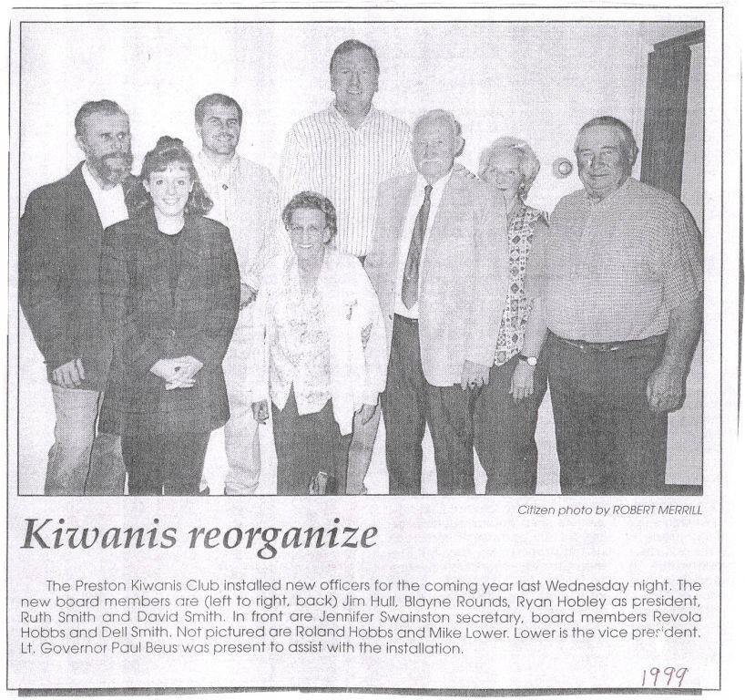 Eight people are standing in a group, posing for a picture. A man and a woman are in the front row, while six people stand behind them. Below the image, there is text titled "Kiwanis reorganize." The text describes the installation of new officers for the Preston Kiwanis Club, listing their names and roles. A note mentions that Lt. Governor Paul Beus assisted with the installation. The year 1999 is handwritten in the bottom right corner.