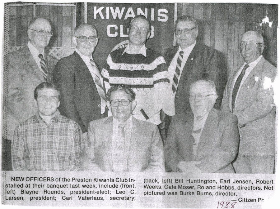 A group of eight men are standing and sitting in a formal setting. Behind them is a banner that reads "Kiwanis Club." A caption below identifies them as new officers of the Preston Kiwanis Club: Blayne Rounds, Leo C. Larsen, Carl Vaterlaus, Bill Huntington, Earl Jensen, Robert Weeks, Gale Moser, and Roland Hobbs. It notes that Burke Burns is not pictured. The year 1988 is noted.