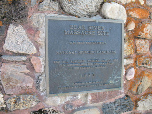 A plaque mounted on a stone wall. The plaque reads: "Bear River Massacre Site has been designated a National Historic Landmark. This site possesses national significance in commemorating the history of the United States of America. 1990. National Park Service, United States Department of the Interior."