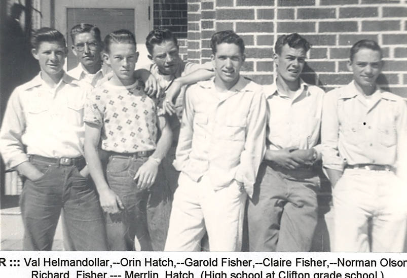 Seven young men standing in a row in front of a brick wall, some with arms around each other's shoulders. They are dressed in casual attire with collared shirts and jeans. Below them, text reads: "L to R ::: Val Helmandollar,--Orin Hatch,--Garold Fisher,--Claire Fisher,--Norman Olson,--Richard Fisher---Merrlin Hatch (High school at Clifton grade school)."
