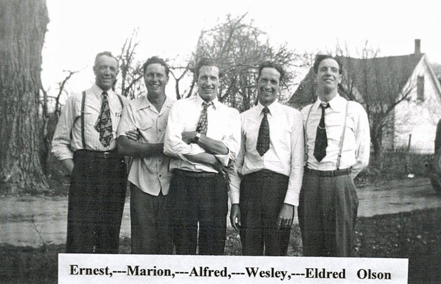 Five men standing in a row outdoors, next to trees and a house. They are wearing dress shirts and ties, some with suspenders. The text below them reads: "Ernest, --- Marion, --- Alfred, --- Wesley, --- Eldred Olson".