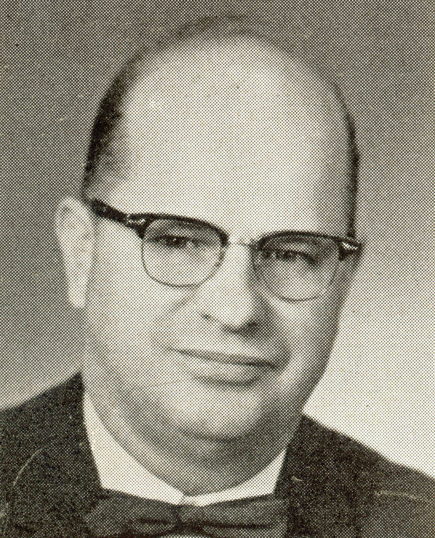 A man with glasses and a bow tie is looking at the camera. He has a bald head and is wearing a collared shirt.