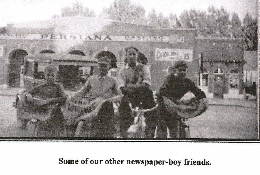 Four boys are standing with their bicycles, each holding a newspaper in the baskets. Behind them is an old vehicle and a building with the sign "PERSIANA." In the background, another sign reads "DANCES 13." Trees are visible beyond the building. Below, a caption reads "Some of our other newspaper-boy friends."
